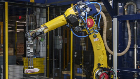 Il nuovo braccio robotico Sparrow, immortalato in diverse posizioni, solleva dei piccoli oggetti da quattro contenitori di plastica grigia allineati davanti a lui