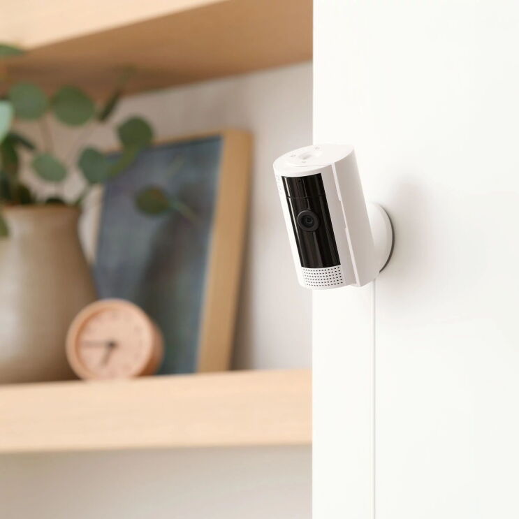 本棚の横の壁に取り付けられている白い円筒形のセキュリティカメラ。Amazon Ring