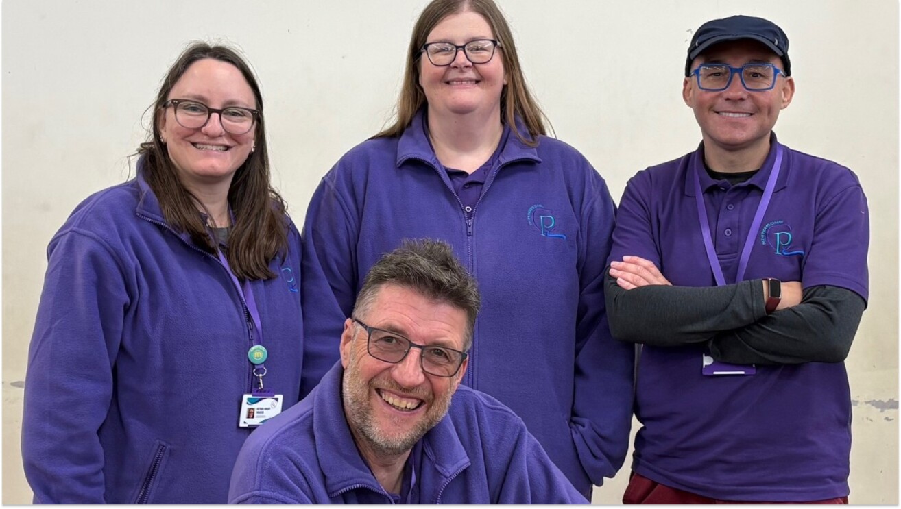 Four smiling staff members in purple uniforms with 'PL' logo