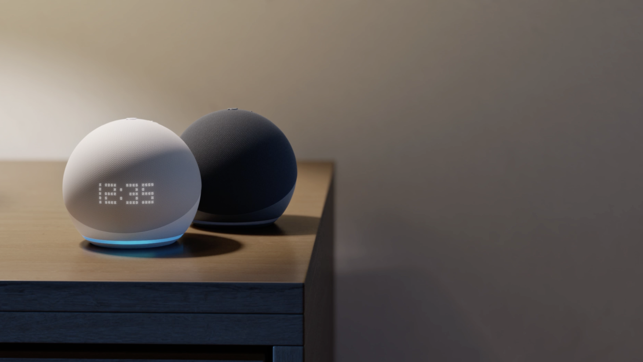 Due dispositivi Echo su un tavolo. Un dispositivo è grigio e ha il display con l'orologio acceso. L'altro è nero ed è in secondo piano. 