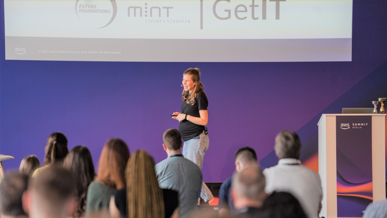AWS GetIT Botschafterin Anja Blank auf der Bühne beim Erklären auf dem AWS Summit 2022 in Berlin worum es bei AWS GetIT geht.