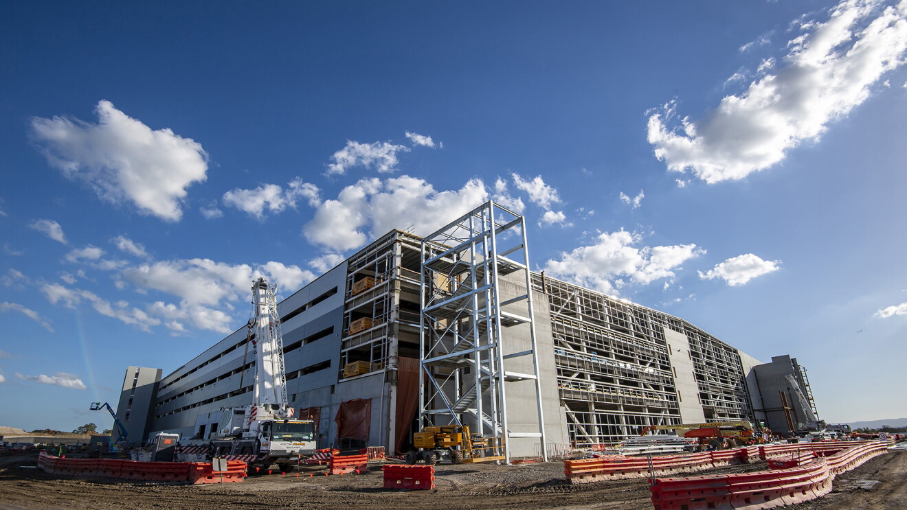 An image of a partially built Amazon fulfillment center with construction barriers and equipment around it. There is a blue sky overhead.