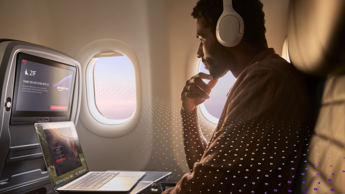 Man sitting on Delta flight with laptop and headphones using Amazon Leo Wi-Fi