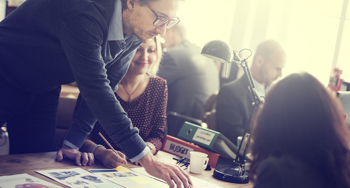 Mitarbeitern diskutieren am Tisch. Ein Mitarbeiter zeigt auf eine Grafik.