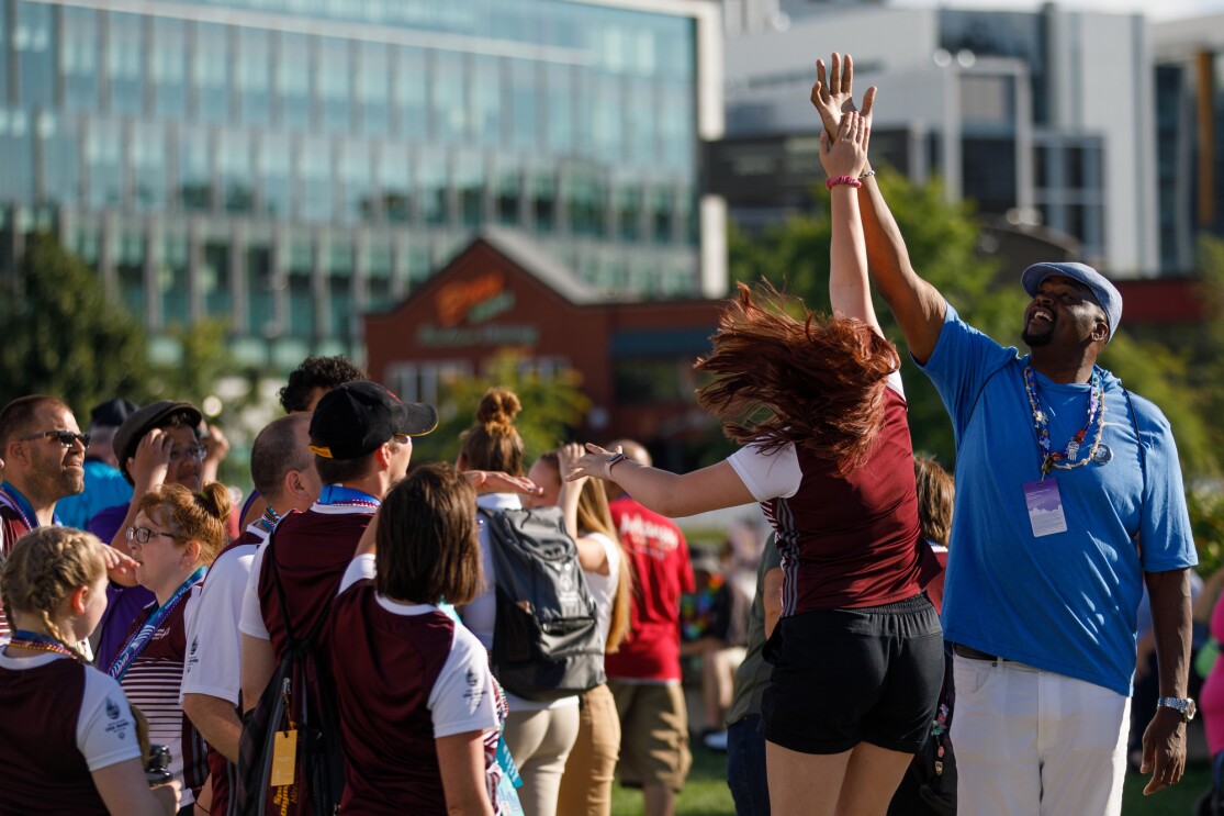 A high five is given at the Special Olympics closing ceremony. To make the high-five happen, a woman is jumping up to reach the hand of a male volunteer's hand.