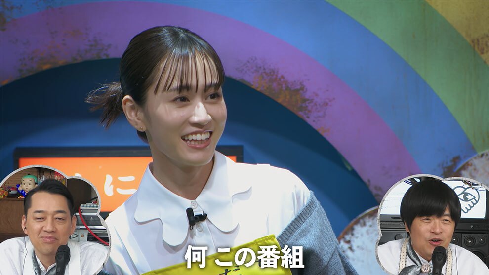 虹色だが表面が荒れた壁を背景に、白いシャツを着た人物の上半身、戸惑うような笑顔。下部に「何 この番組」というテロップが出ている。字幕を挟んで左右両端の囲み内に、マイクを前にした設楽統氏とバカリズム氏がモニタリングしている。