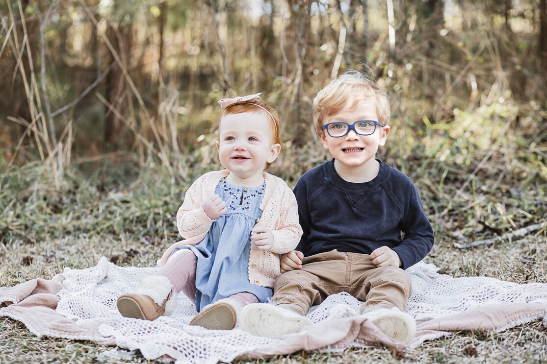 An image of two children sitting on a blanket outside smiling for a professional photo.