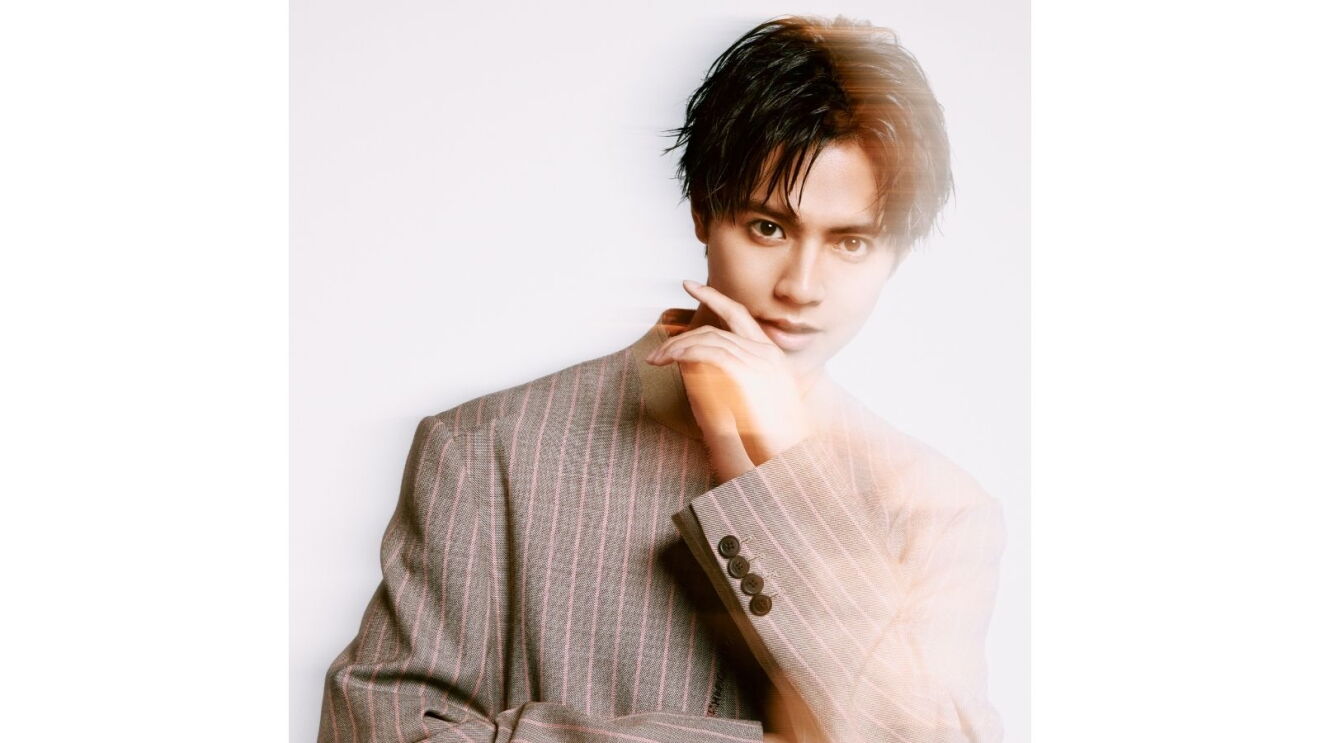 茶色のストライプのジャケットを着ている男性(片寄涼太さん)がほほに左手をあててほほ笑んでいる