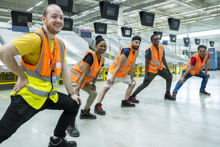 5 Mitarbeiter:innen bei Amazon bei Dehnübungen in der Logistikhalle.