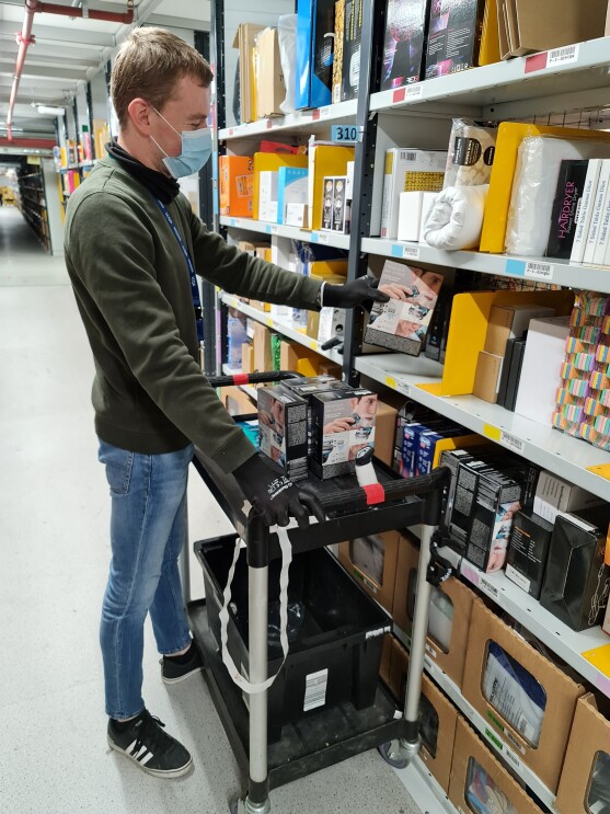 Amazon employee, Raimonds Duboks adding products to a shelf whilst on a ladder and wearing a mask