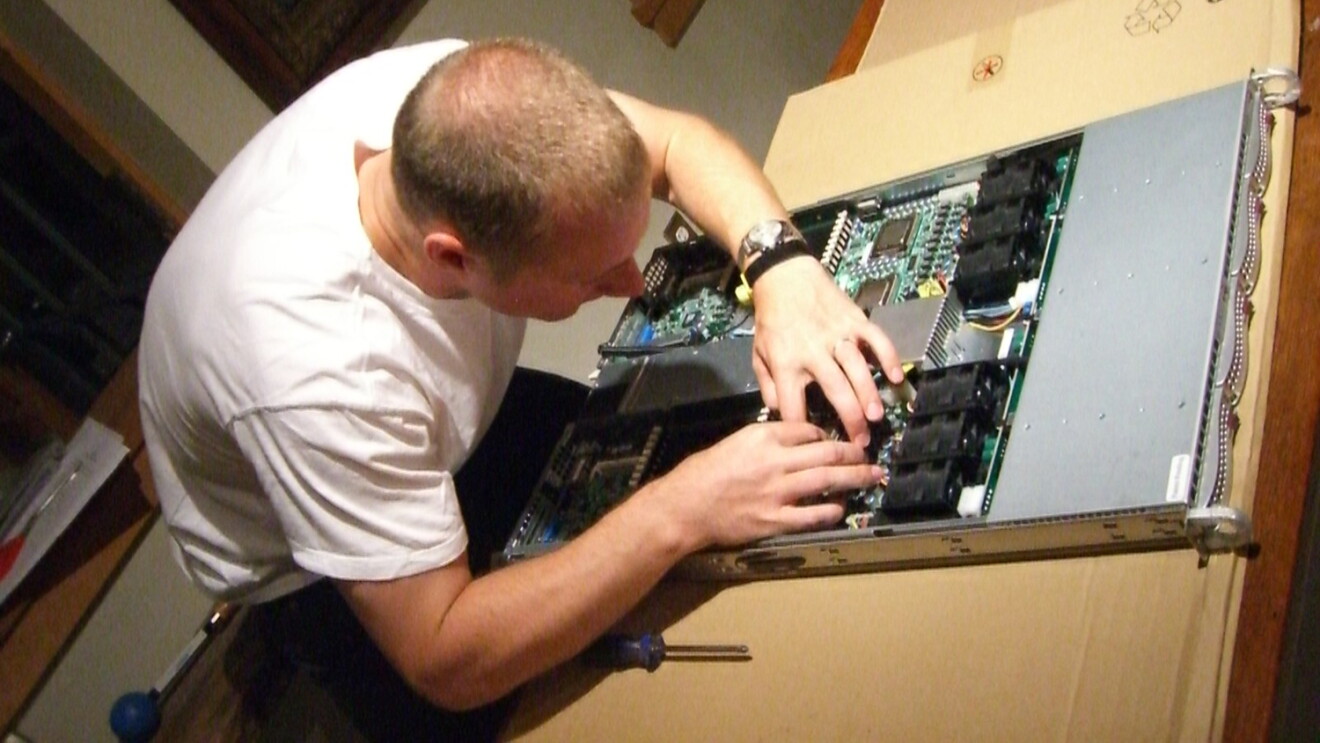 An image of a man working on the motherboard of a computer in a low-lit room. 