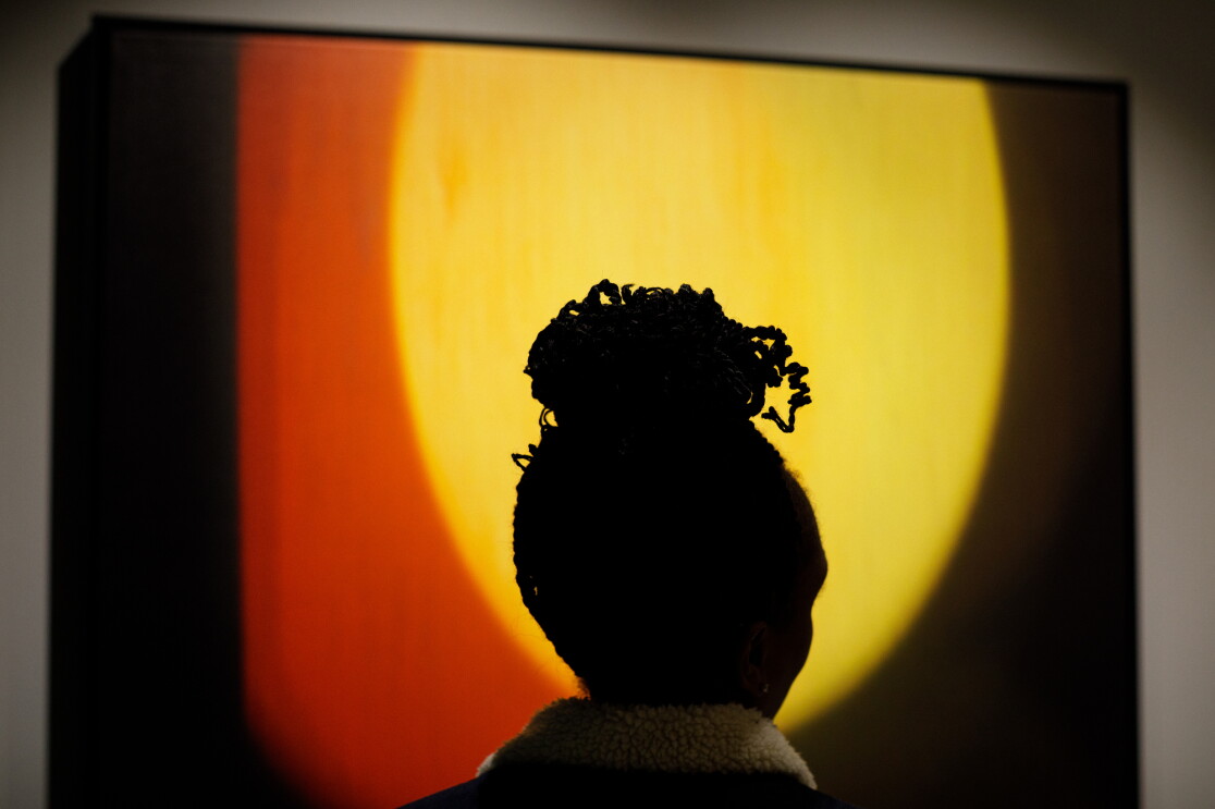 A silhouetted woman stares at a piece of art. The art is a yellow circle with an orange border on a black canvas.