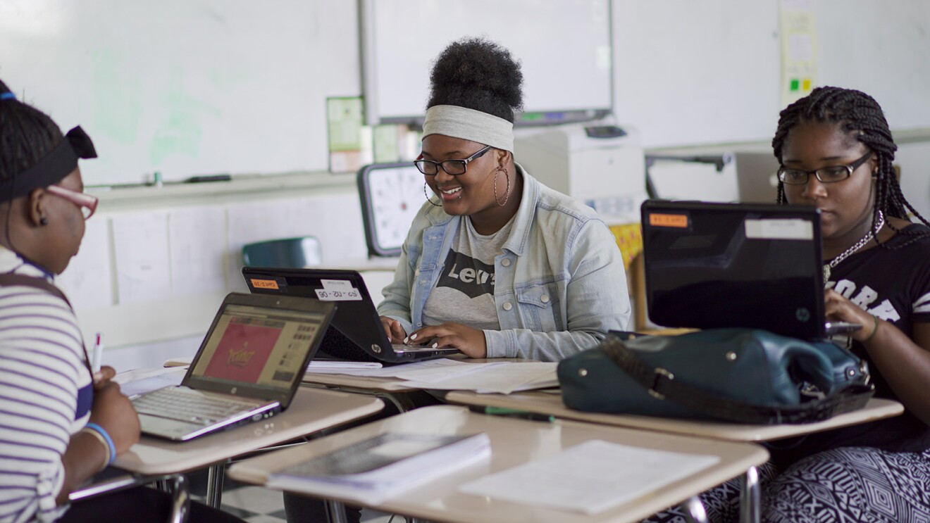 A photo of three students sitting at their desks, working on laptop devices.