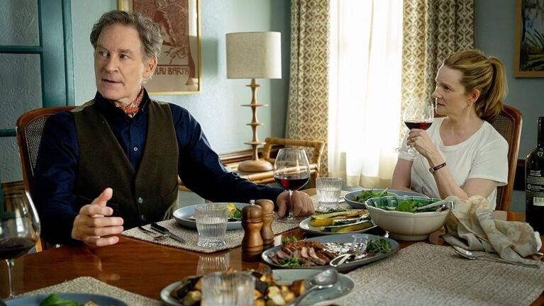 Man and woman share a meal at a table in a home, each with a glass of wine 