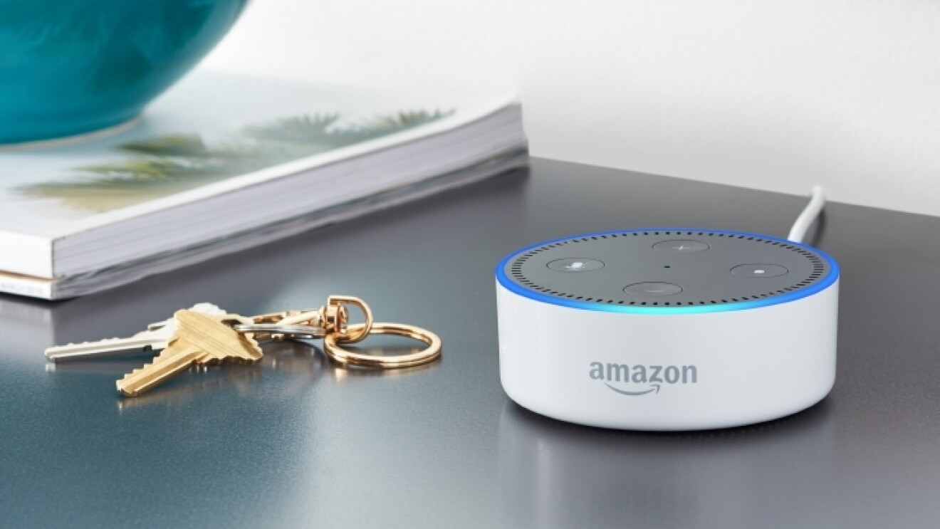 A white Amazon Echo Dot on a night stand, next to a pair of keys.