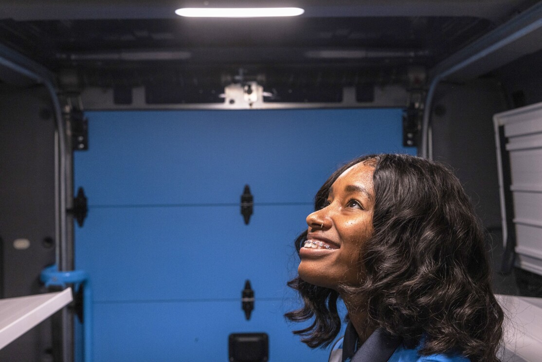 A photo of the head of a delivery driver standing inside the storage space of an Amazon delivery van from Rivian, with the roof a few feet above their head.