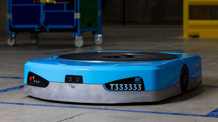 An image of Amazon's new Titan robot. It's blue, plate-like robot with black details, including a camera on the front, a name plate that says "T333333" and a large, circular plate on top.