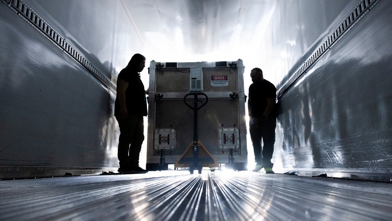 An image of two men pushing a Project Kuiper shipping container into a truck.