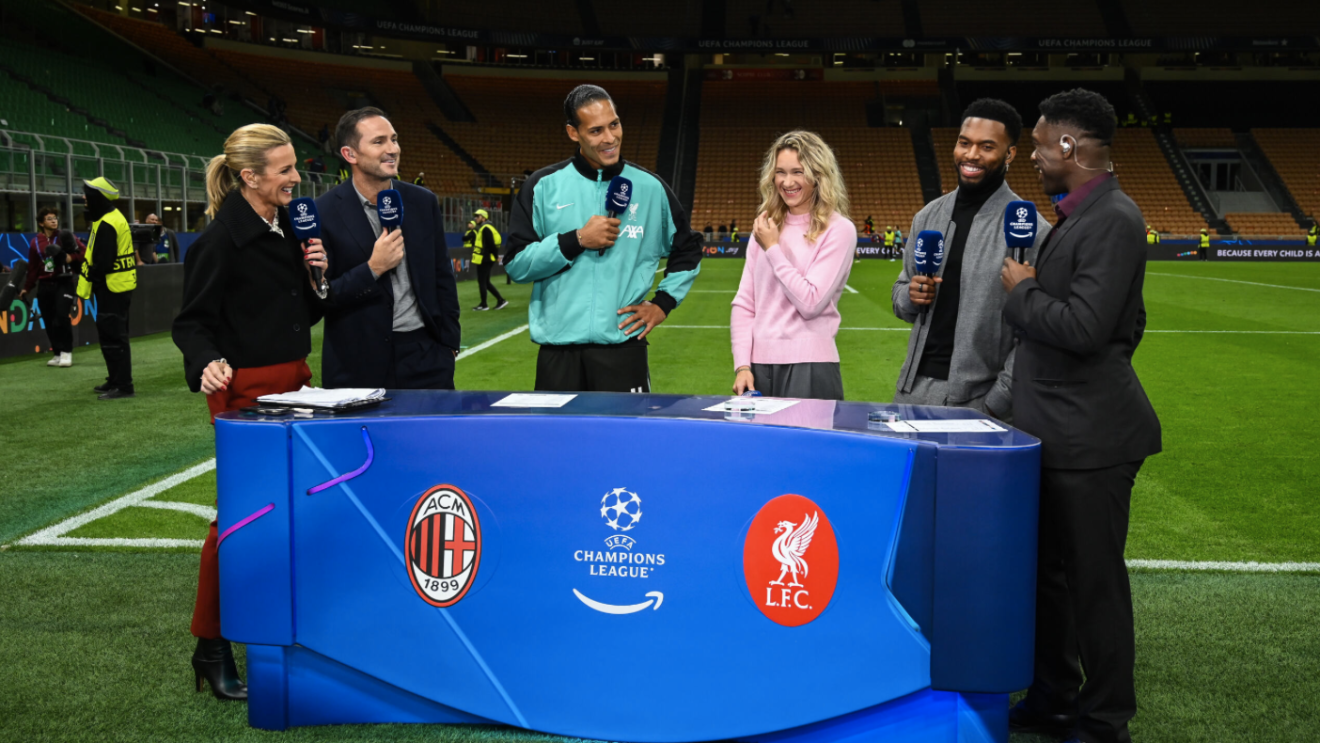 A still from Prime Video's coverage of the Champions League, showing pundits behind a pitch-side desk with microphones