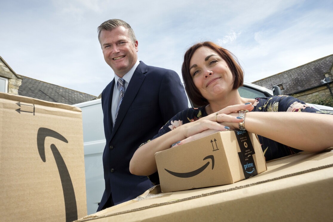 James and Rebecca, owners of JMHC Logistics, standing behind Amazon boxes.