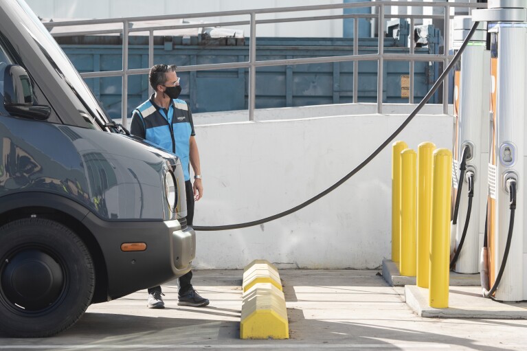 An Amazon-branded Rivian van gets charged at an electric station by a man wearing a face mask during the pandemic.