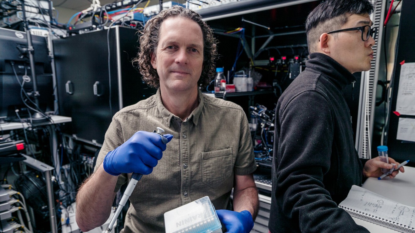 A photo of Ed Lein, Ph.D. of the Allen Institute for Brain Science standing in a lab, holding a micropipette. 