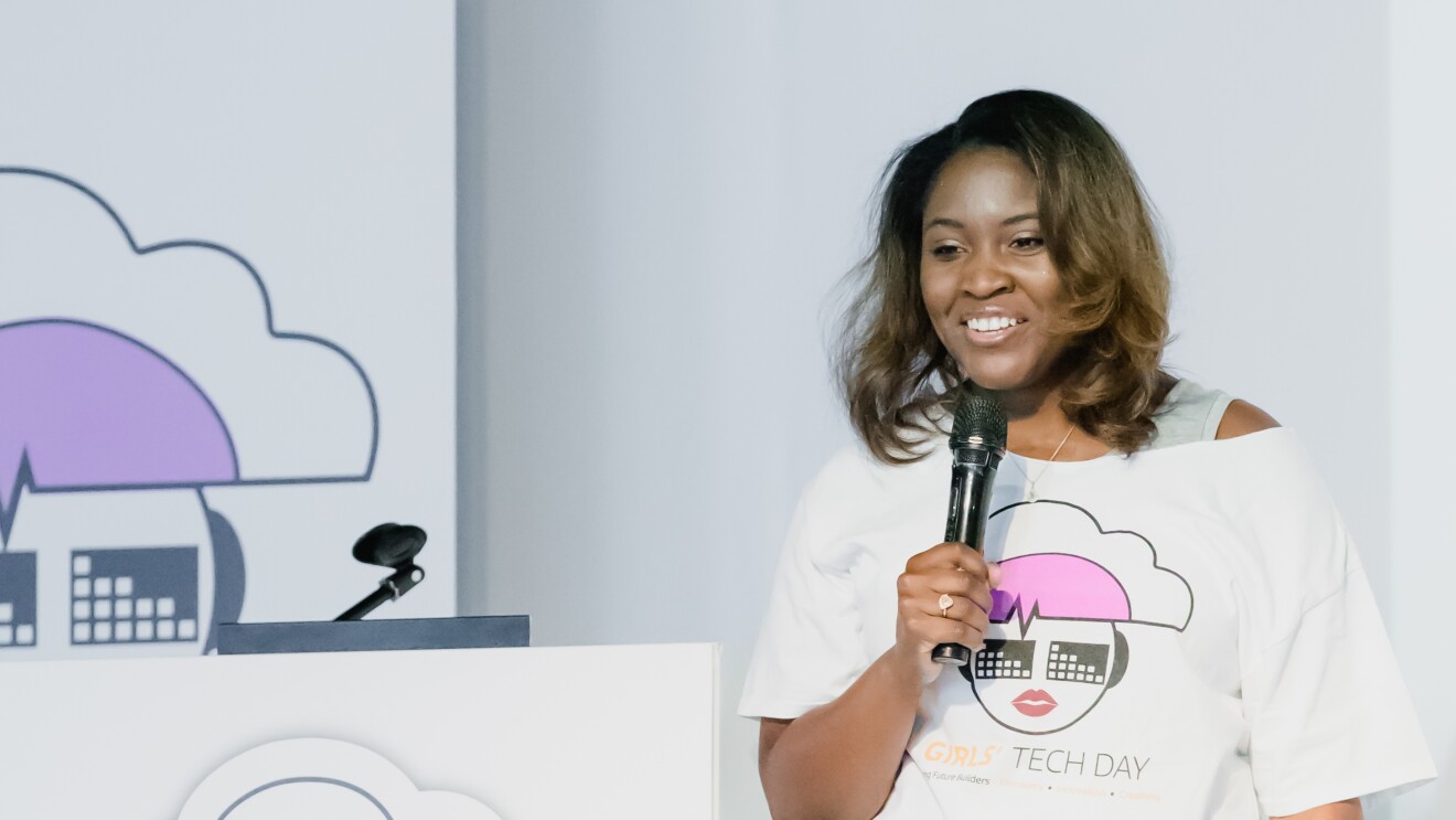 Cornelia Robinson, Global Leader of AWS InCommunity holding a microphone and wearing a Girls' Tech Day T-shirt speaks at an AWS InCommunity event