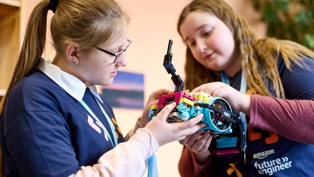 Zwei Schüler:innen arbeiten beim FIRST LEGO League Wettbewerb an ihrem Roboter und Forschungsprojekt. Auf der T-Shirt einer Schülerin ist Amazon future engineer geschrieben.