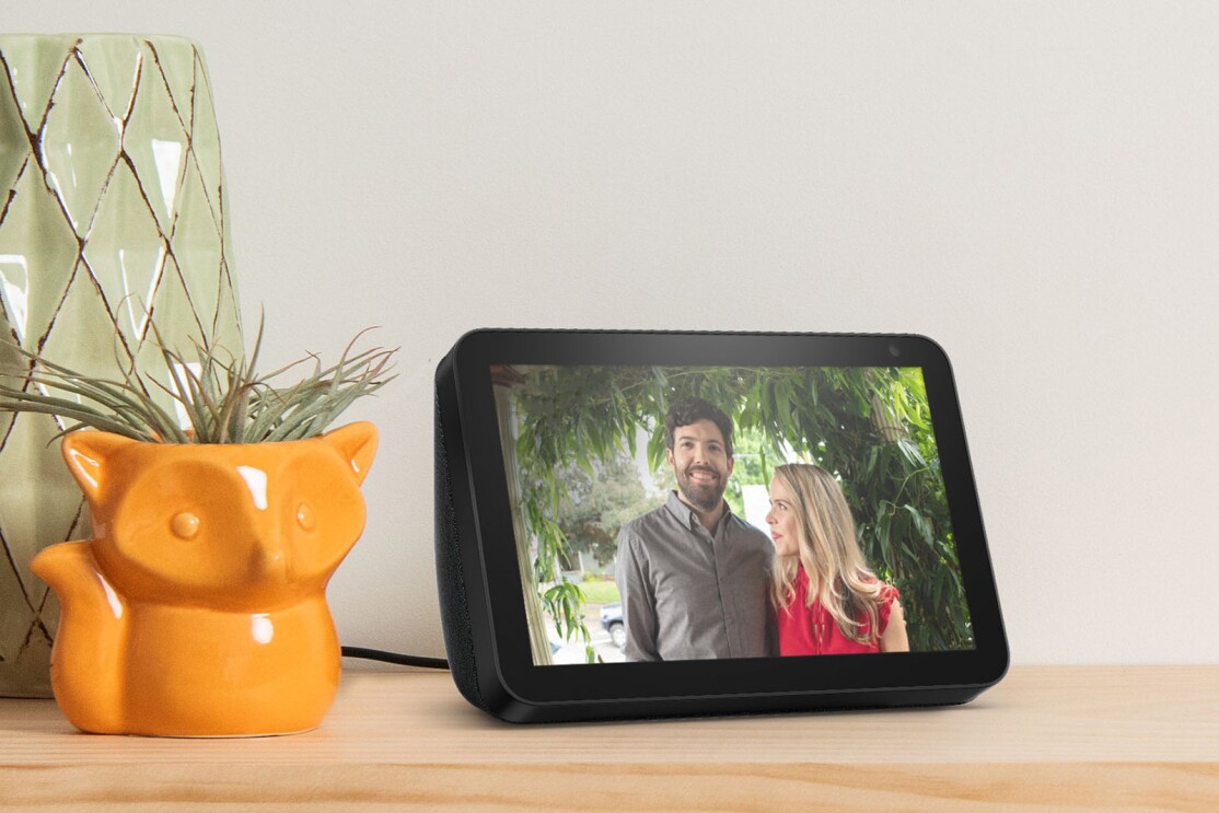 An image of an Echo Show device sitting on a kitchen counter. Next to it is an orange vase in the shape of a fox with a succulent coming out the top. There is another light green vase behind it.