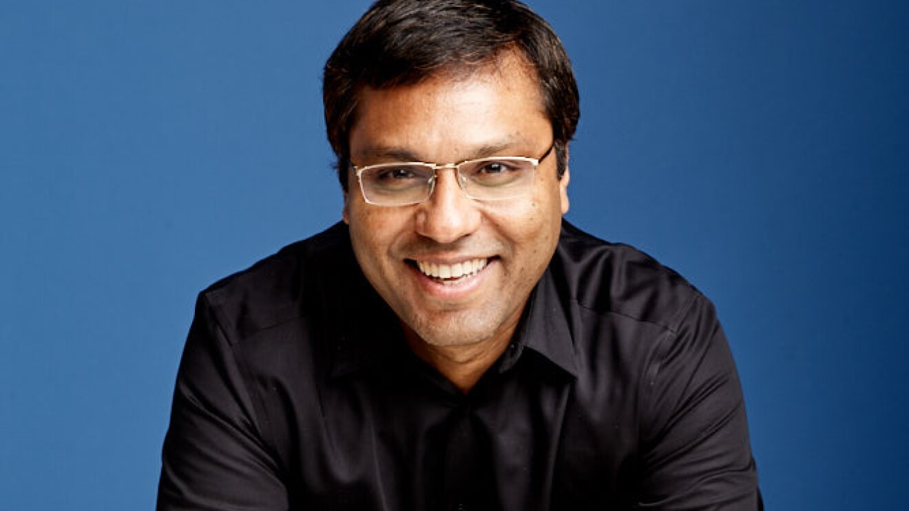 A portrait of Rohit Prasad, vice president and head scientist, Alexa AI. He is wearing a black shirt and is photographed against a blue background.