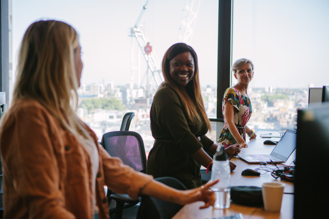 Three female employees stood at their desks, looking happy whilst working at Amazon head office 