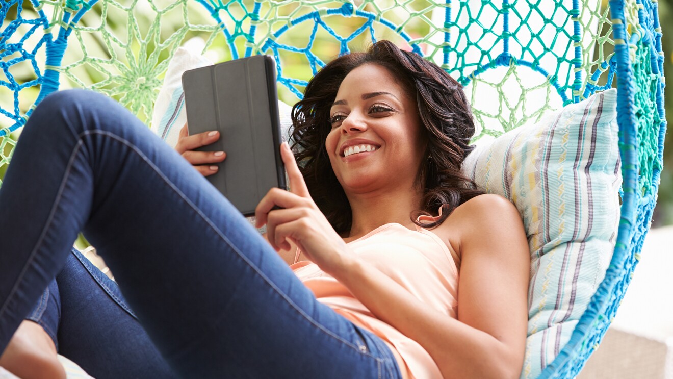 一名女子躺在秋千上看平板电脑上的内容。”width=