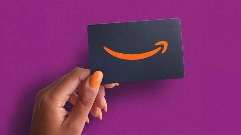 A hand with orange nail polish holding up an Amazon gift card against a purple background