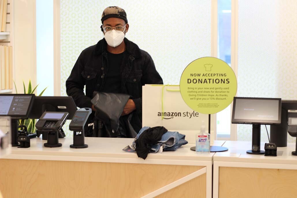 An image of a cashier folding a pleather blazer. There is an Amazon Style bag next to him on the counter where he will place the clothing once it's folded. 