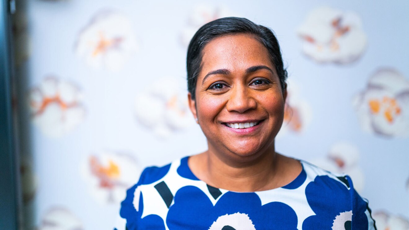 An image of a woman smiling for a headshot photo. Behind her is wallpaper with large pieces of popcorn pictured on it.