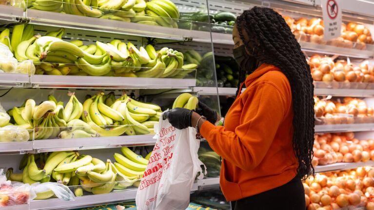 Woman in orange hoodie and mask choosing fruit from display