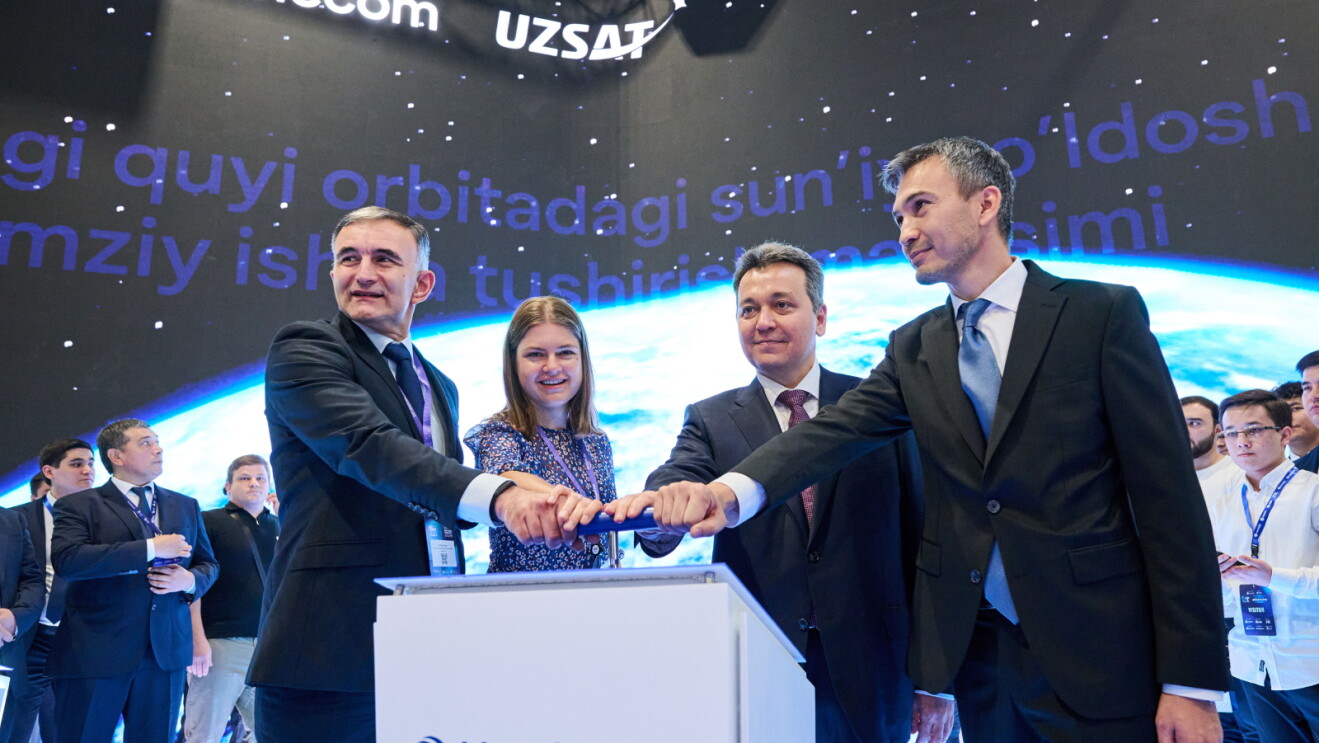 Three men and a woman in business attire at an event, pushing down together on a lever