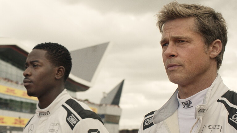 Two race car drivers in white uniforms standing at a racing circuit