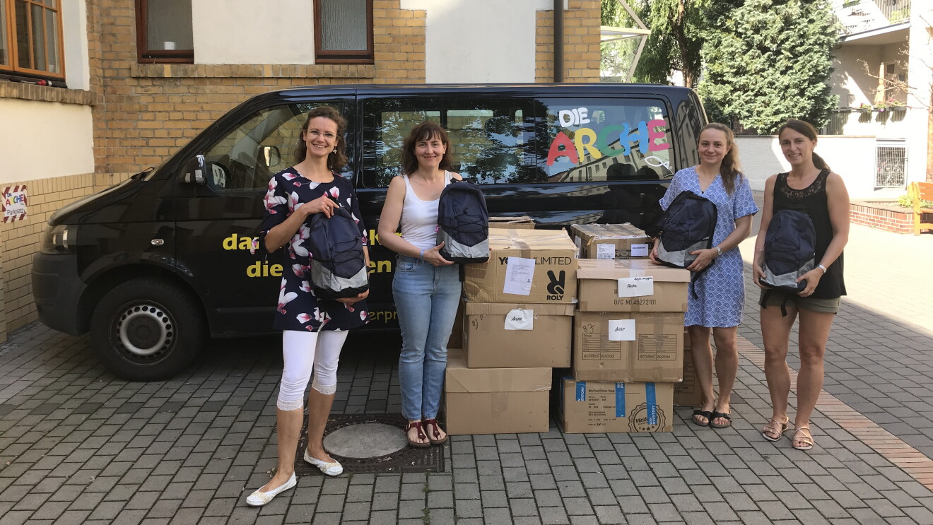Volunteers von Amazon mit gespendetem Schulmaterial und Kisten vor einem Van der Arche.