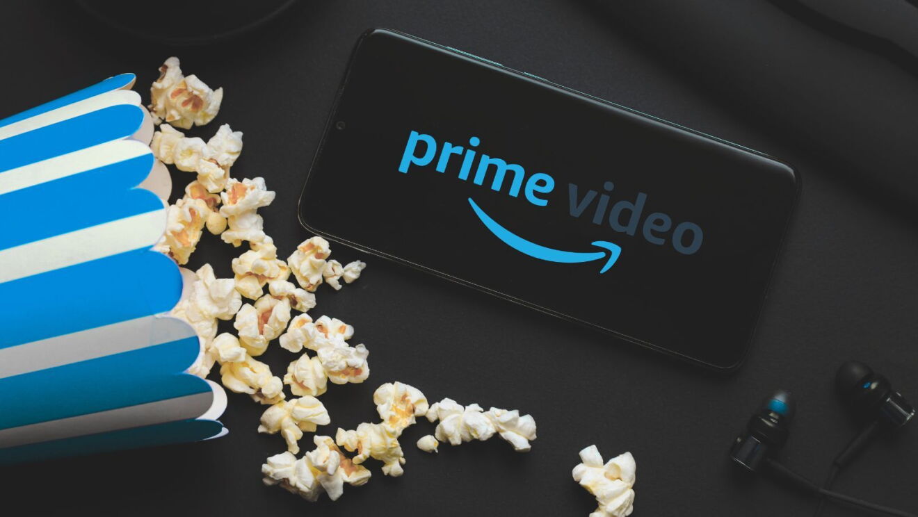 Flatlay of a mobile phone showing the words 'Prime Video' next to a blue-striped tub of popcorn and a pair of earphones.