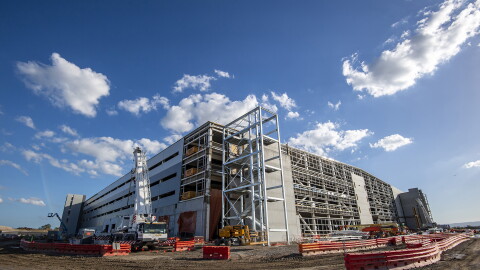 An image of a partially built Amazon fulfillment center with construction barriers and equipment around it. There is a blue sky overhead.