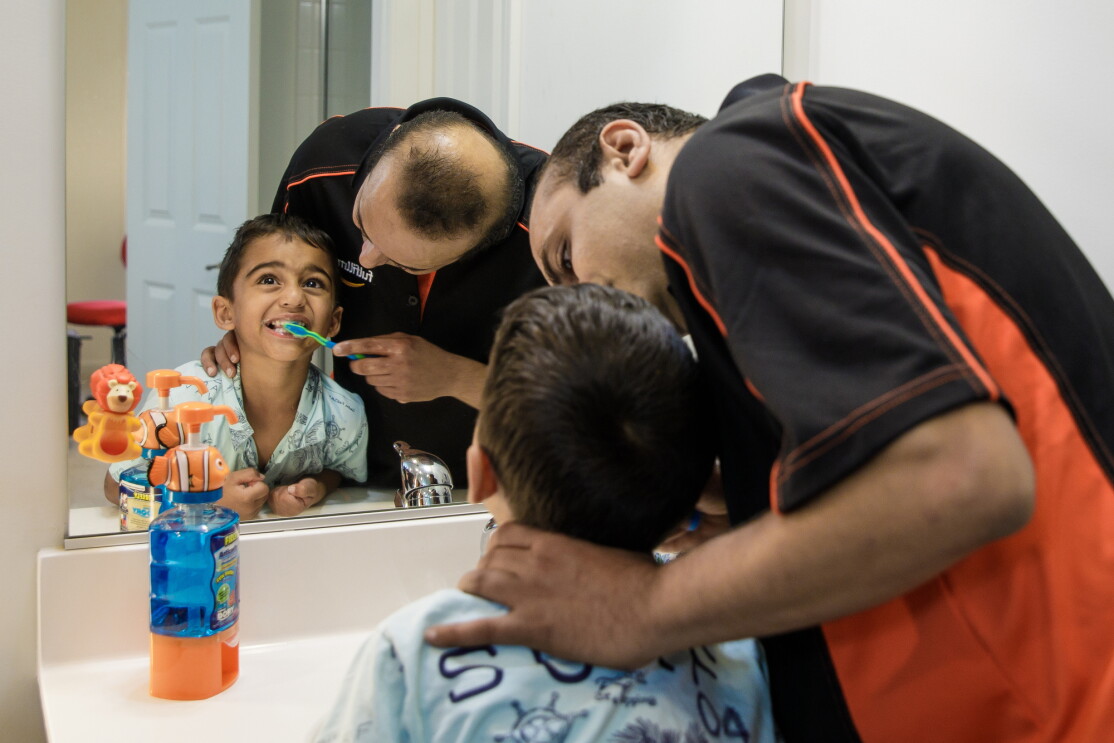 A man brushes a young boy's teeth in a bathroom. 