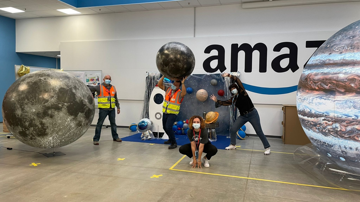 Gruppo di dipendenti Amazon posa in mezzo a riproduzioni di pianeti. 