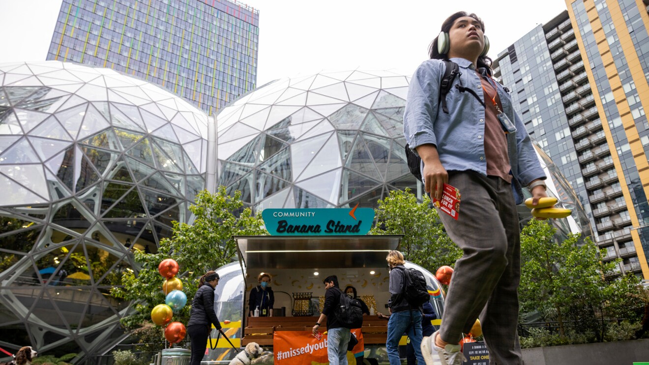 A photo of an employee walking outside at Amazon's Seattle headquarters, with the banana stand and spheres behind them.