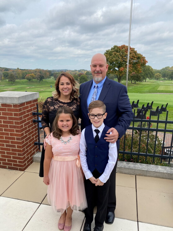 A family of four stand on a pavilion, dressed up, and smile at the camera.
