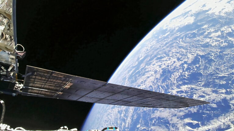 Solar panel of space station extending over curved Earth surface