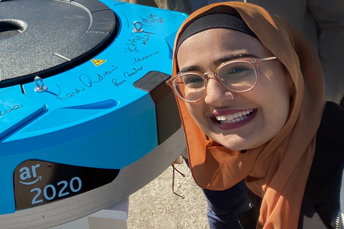 A woman poses with an Amazon Robotics unit.