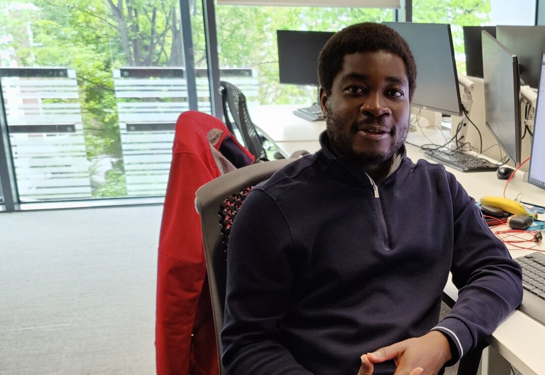 An image of a man smiling for a photo while sitting at a desk at an office. 