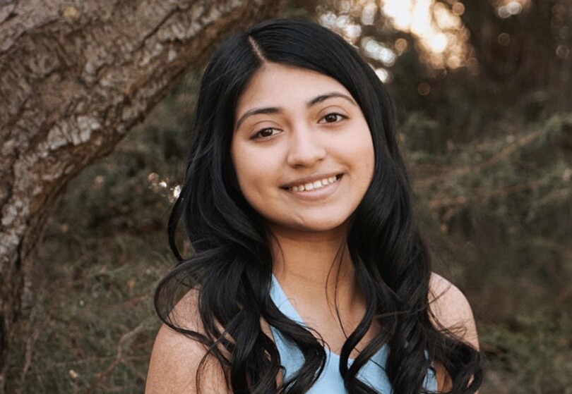 An image of a young woman smiling for a headshot photo in a wooded area.