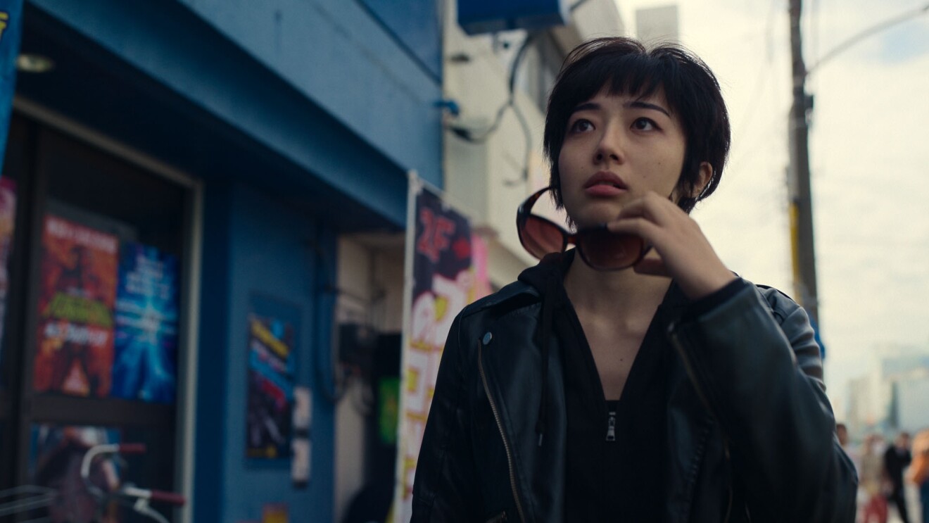 繁華街でサングラスを外し、上方を見つめるショートカットの女性